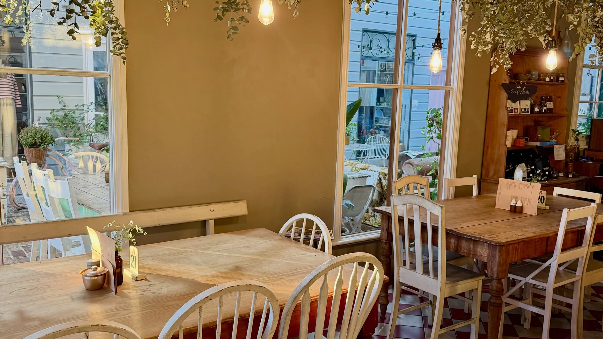 Window light falls across timber tables, hanging greenery and the café's red and cream checkerboard floor